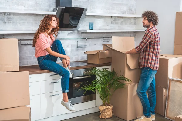 Side view of couple unpacking cardboard boxes at new home and looking at each other — Stock Photo