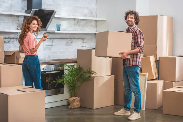 Smiling couple unpacking cardboard boxes at new kitchen and looking at camera — Stock Photo