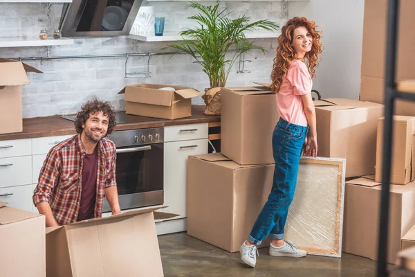 Smiling couple unpacking cardboard boxes at new home and looking at camera — Stock Photo