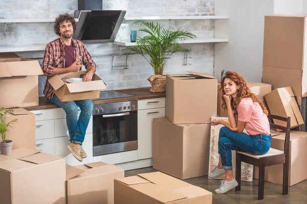 Couple unpacking cardboard boxes at new home and looking at camera — Stock Photo