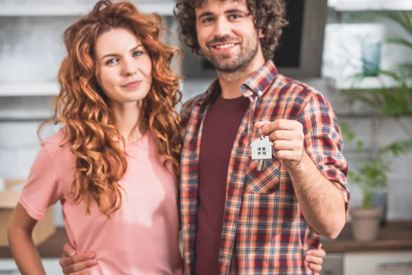 Ritratto della coppia sorridente che abbraccia e tiene il gingillo della casa con le chiavi a nuova casa — Foto stock