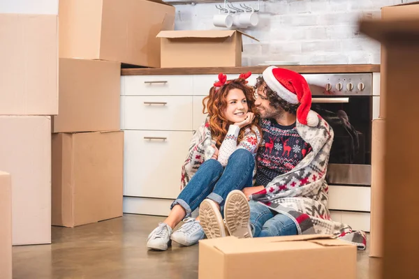 Feliz jovem casal sorrindo uns aos outros enquanto sentado entre caixas de papelão no Natal — Fotografia de Stock