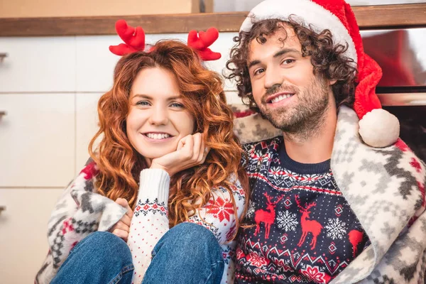 Happy young couple in santa hat and antlers headband smiling at camera together — Stock Photo