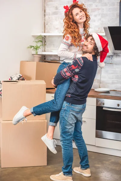Feliz jovem casal abraçando e sorrindo para a câmera ao se mudar na época do Natal — Fotografia de Stock