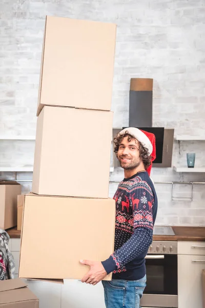 Красивий щасливий чоловік у капелюсі Санта тримає картонні коробки і посміхається на камеру — стокове фото