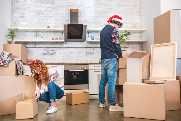 Young couple unpacking cardboard boxes in new apartment at christmastime — Stock Photo