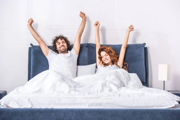 Feliz jovem casal esticando os braços e acordar juntos no quarto — Fotografia de Stock