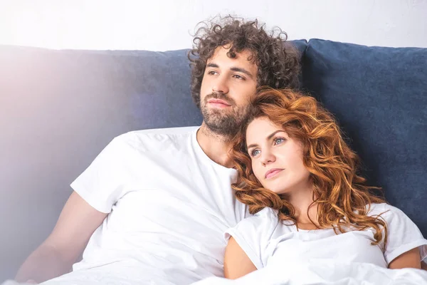 Pensive young couple looking away while lying together in bed — Stock Photo