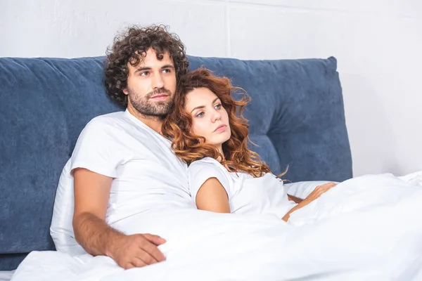 Красивая молодая пара лежит вместе на кровати и смотрит в сторону — стоковое фото