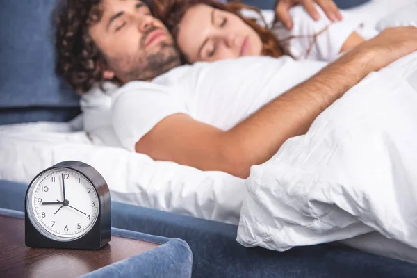 Vue rapprochée du réveil et du jeune couple couchant ensemble derrière — Photo de stock