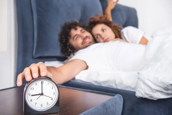 Close-up vista de despertador e jovem casal acordar juntos — Fotografia de Stock