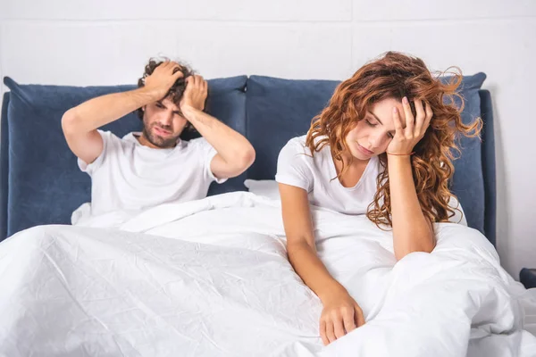 Молодая пара сидит на кровати и страдает от головной боли по утрам — стоковое фото