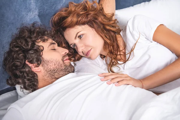 Sorrindo jovem olhando para namorado dormindo na cama — Fotografia de Stock