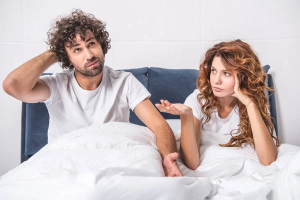 Jovem casal com dor de cabeça sentado juntos na cama — Fotografia de Stock