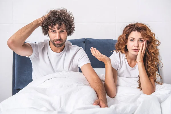 Junges Paar mit Kopfschmerzen sitzt auf dem Bett und blickt in die Kamera — Stockfoto