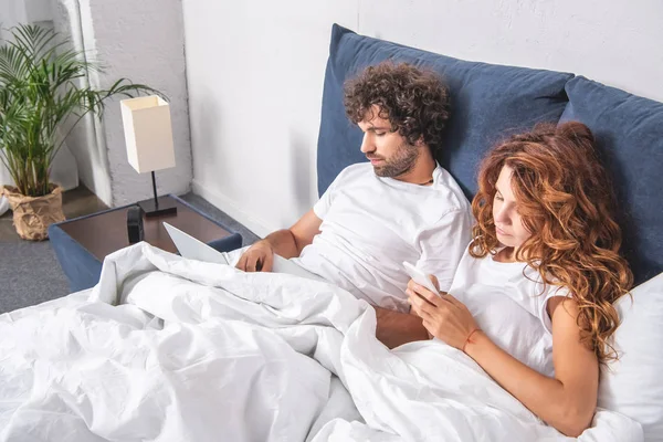 High angle view of young couple lying in bed and using digital devices — Stock Photo