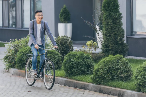 Elegante sonriente asiático hombre ciclismo en bicicleta en la ciudad - foto de stock