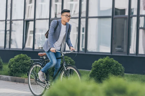 Stylish asian man in gray jacket biking in city — Stock Photo
