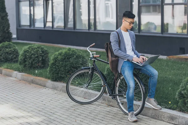 Confident asian freelancer using laptop while sitting on bicycle — Stock Photo