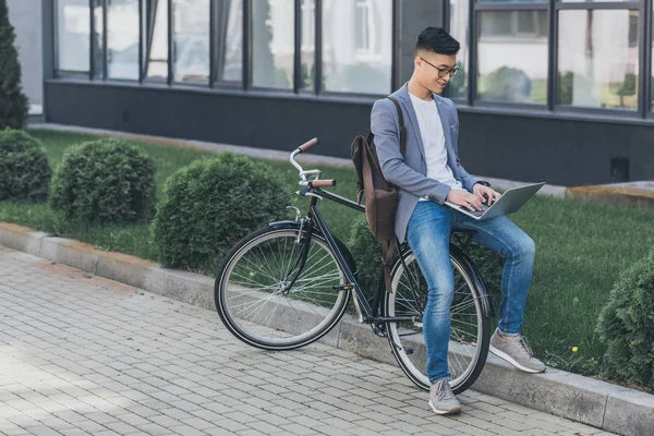 Stylish asian freelancer using laptop while sitting on bike — Stock Photo