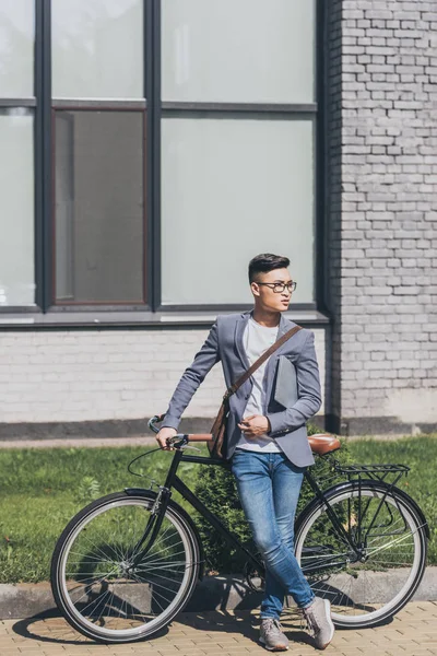 Handsome confident asian man with laptop standing at bike — Stock Photo