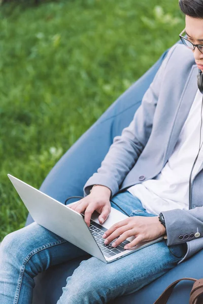 Freelancer asiático trabalhando no laptop enquanto sentado na cadeira de saco de feijão no gramado — Fotografia de Stock