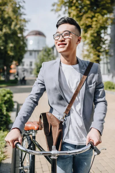 Feliz guapo asiático hombre caminando con bicicleta en ciudad - foto de stock