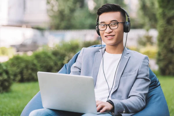 Sourire asiatique homme télétravail sur ordinateur portable tout en étant assis sur haricot sac chaise — Photo de stock