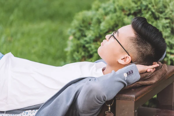 Стильный азиатский мужчина в очках спит на скамейке запасных — стоковое фото
