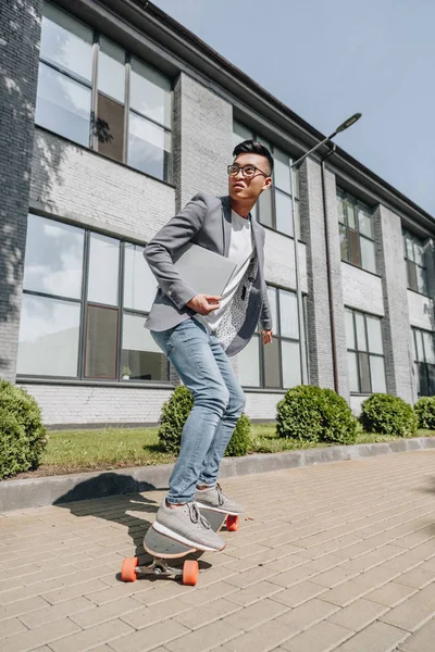 Handsome asian man with laptop skateboarding on longboard — Stock Photo