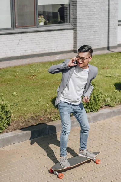 Азиатский человек с ноутбуком, беседующий во время езды на длинной доске на улице — стоковое фото