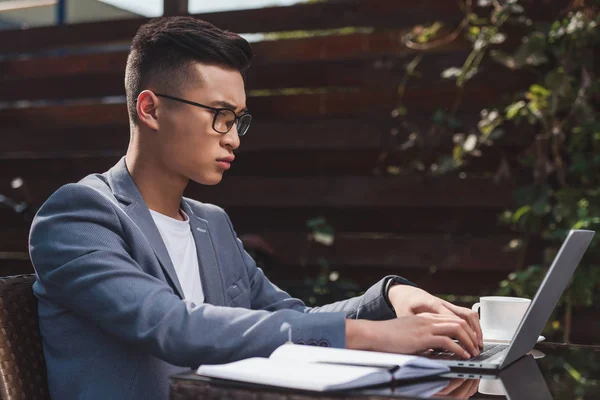 Side view of concentrated asian businessman remote working on laptop in cafe — Stock Photo