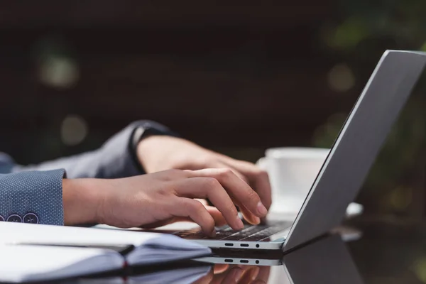 Cropped shot of businessman typing on laptop at tabletop with notebook — Stock Photo