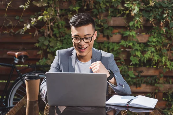 Feliz asiático hombre de negocios mirando portátil pantalla en mesa con café para ir - foto de stock