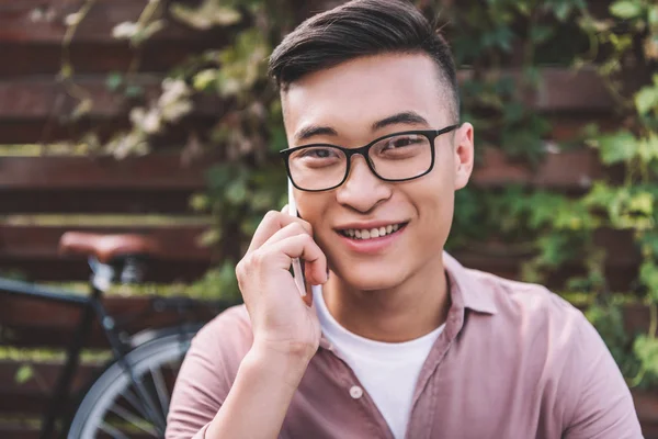 Portrait of smiling asian man in eyeglasses talking on smartphone — Stock Photo