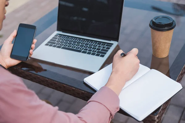 Teilbild eines Mannes mit Smartphone-Fernbedienung, der am Tisch mit Coffee to go arbeitet — Stockfoto