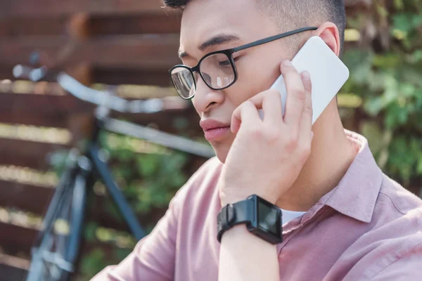 Focused asian man in eyeglasses talking on smartphone — Stock Photo