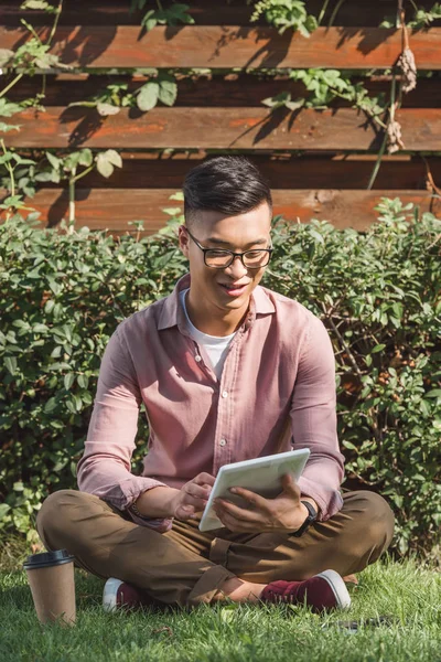 Jovem asiático homem usando digital tablet no verde grama no parque — Fotografia de Stock