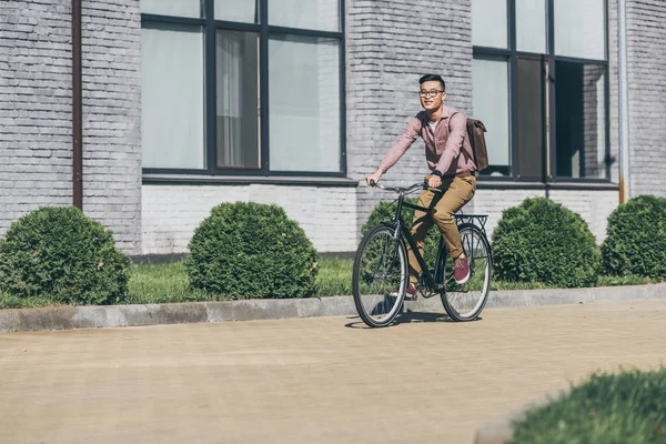 Asian young man with backpack riding bicycle on street — Stock Photo
