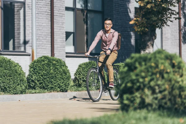 Азиатский молодой человек с рюкзаком езда на велосипеде на улице — стоковое фото