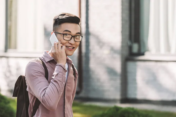 Side view of asian young man in eyeglasses having conversation on smartphone on street — Stock Photo