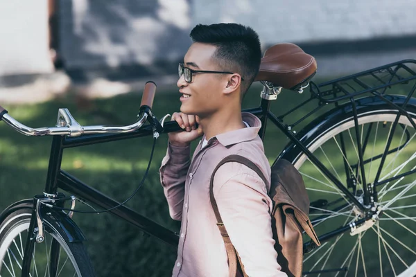 Улыбающийся азиатский мужчина с велосипедом во время прогулки по улице — стоковое фото