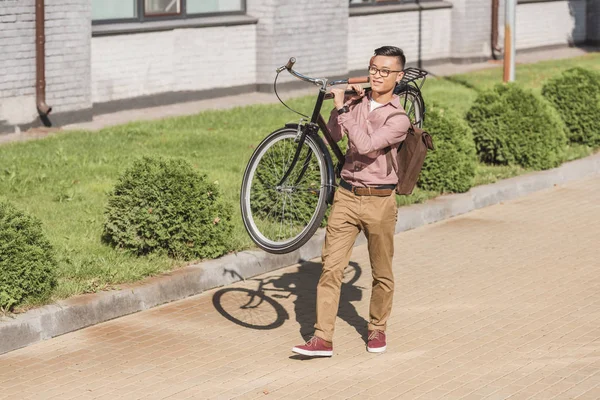 Asian man with backpack carrying bicycle while walking on street — Stock Photo