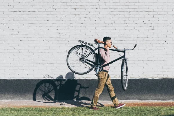 Side view of asian man carrying bicycle while walking on street — Stock Photo