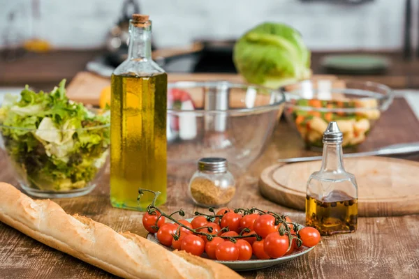 Verduras frescas maduras para ensalada, botella de aceite de oliva y baguette en la mesa en la cocina - foto de stock