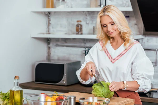 Mulher loira adulta preparando salada para jantar e corte de repolho em casa — Fotografia de Stock