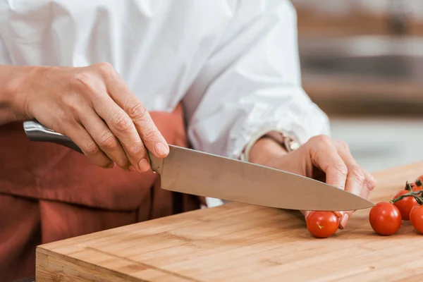 Imagen recortada de la mujer preparando ensalada para la cena y cortando tomates cherry en la cocina - foto de stock