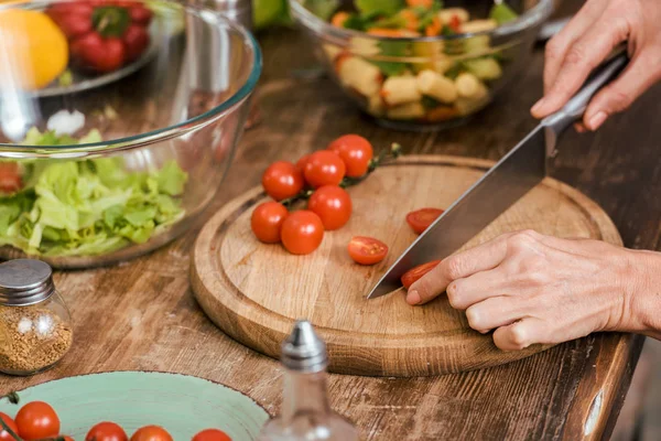 Immagine ritagliata di donna che prepara l'insalata per la cena e il taglio di pomodorini a casa — Foto stock