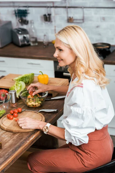 Vue latérale de la femme adulte attrayante préparant la salade pour le dîner à la maison — Photo de stock