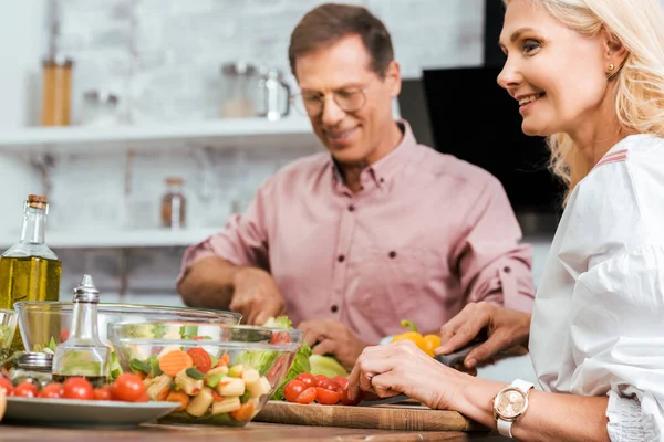 Moglie sorridente e marito preparare insalata per la cena insieme in cucina — Foto stock